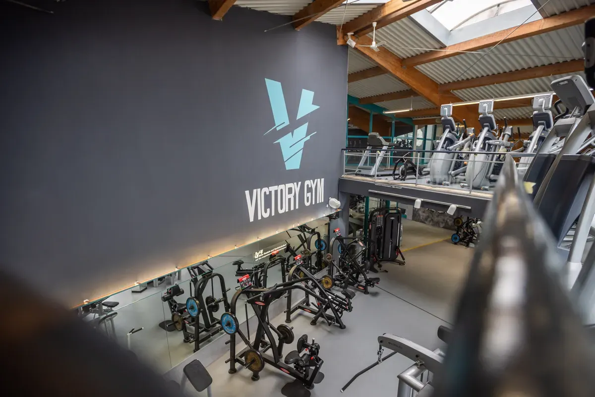 Trainingsbereich mit Geräten unter dem Victory-Gym-Schriftzug an der dunklen Wand